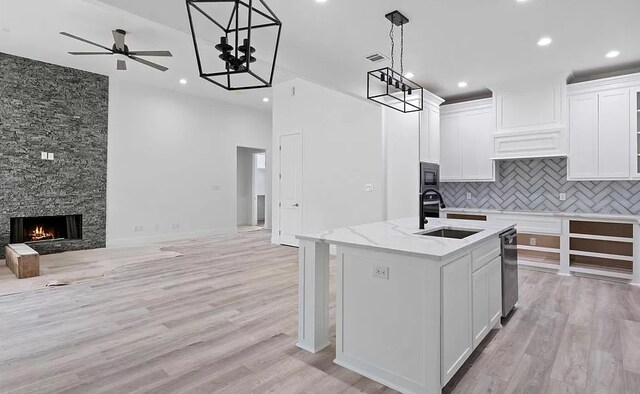 kitchen with a stone fireplace, pendant lighting, white cabinetry, an island with sink, and sink