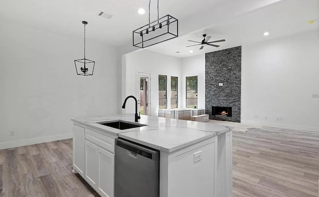 kitchen with pendant lighting, white cabinets, a center island with sink, stainless steel dishwasher, and light stone counters