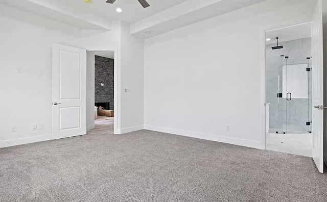 carpeted spare room with ceiling fan and a stone fireplace