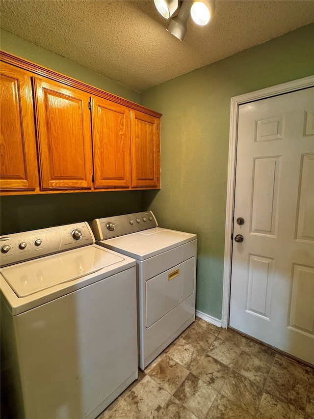 clothes washing area with washer and clothes dryer, cabinets, and a textured ceiling