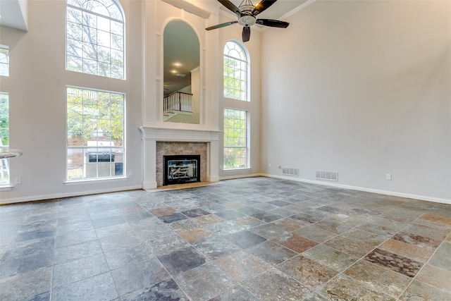 unfurnished living room featuring a healthy amount of sunlight, a towering ceiling, and ceiling fan