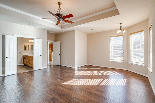 unfurnished room featuring ceiling fan with notable chandelier, a raised ceiling, ornamental molding, and dark wood-type flooring