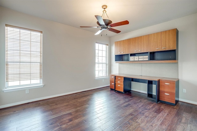 unfurnished office with dark hardwood / wood-style floors, ceiling fan, and built in desk