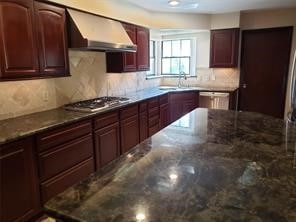 kitchen featuring tasteful backsplash, dark stone countertops, stainless steel appliances, and wall chimney range hood