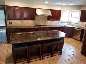 kitchen with appliances with stainless steel finishes, a kitchen island, a breakfast bar area, and wall chimney range hood