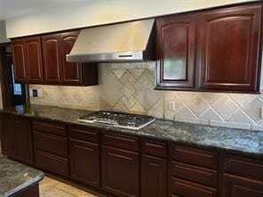 kitchen with backsplash, dark stone counters, wall chimney range hood, and stainless steel gas stovetop