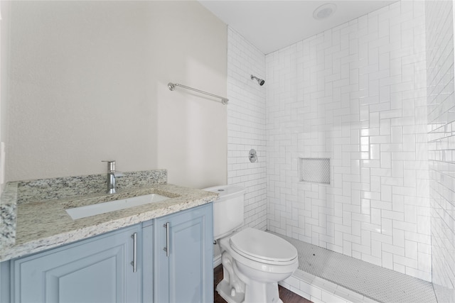 bathroom with a tile shower, vanity, and toilet