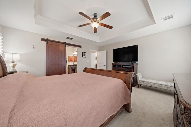 carpeted bedroom featuring ensuite bath, a barn door, ceiling fan, and a tray ceiling