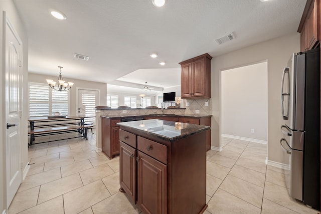 kitchen with stainless steel refrigerator, backsplash, kitchen peninsula, a chandelier, and a kitchen island