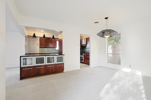 kitchen featuring pendant lighting, wall chimney range hood, backsplash, and light carpet