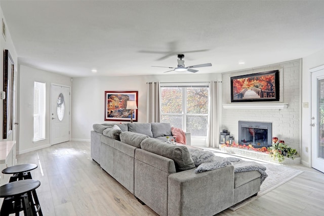 living room with ceiling fan, a brick fireplace, and light wood-type flooring