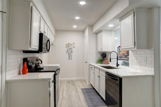 kitchen with tasteful backsplash, white cabinetry, sink, black appliances, and light hardwood / wood-style flooring