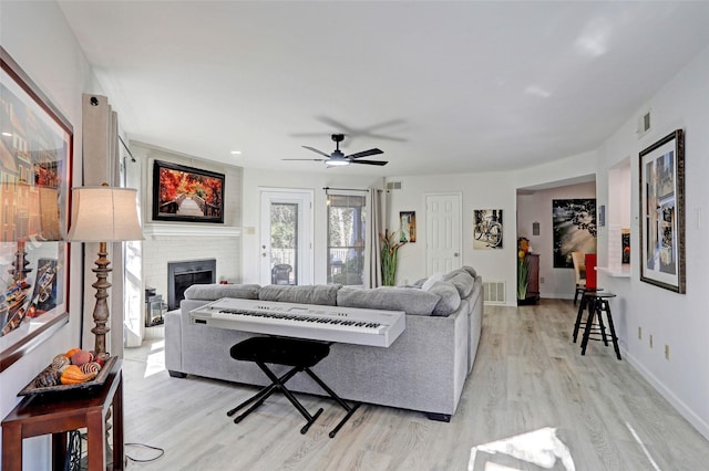 living room with light wood-type flooring, a brick fireplace, and ceiling fan