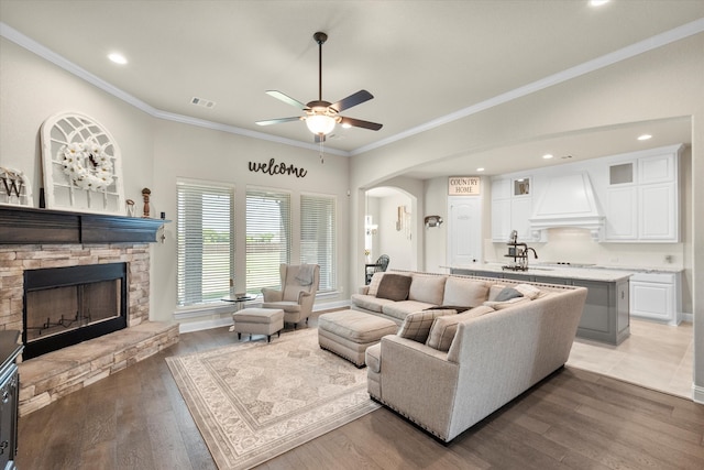 living room with hardwood / wood-style flooring, ornamental molding, ceiling fan, and a fireplace