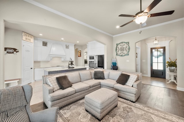 living room with crown molding, ceiling fan, sink, and light wood-type flooring