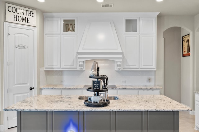 kitchen featuring light stone counters, a kitchen island with sink, and white cabinets