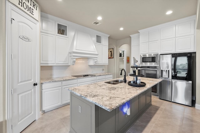 kitchen featuring sink, appliances with stainless steel finishes, white cabinetry, premium range hood, and a center island with sink