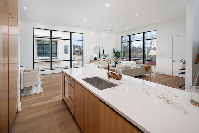 kitchen with a sink, open floor plan, light wood-type flooring, light stone countertops, and modern cabinets