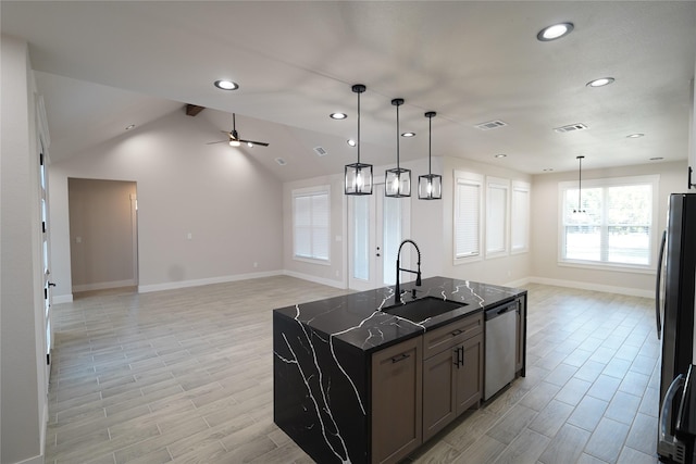 kitchen featuring sink, dark stone counters, hanging light fixtures, stainless steel appliances, and a center island with sink