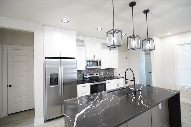 kitchen with sink, stainless steel appliances, an island with sink, dark stone counters, and pendant lighting