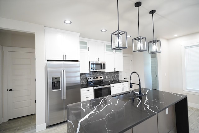 kitchen featuring sink, decorative light fixtures, dark stone counters, an island with sink, and stainless steel appliances