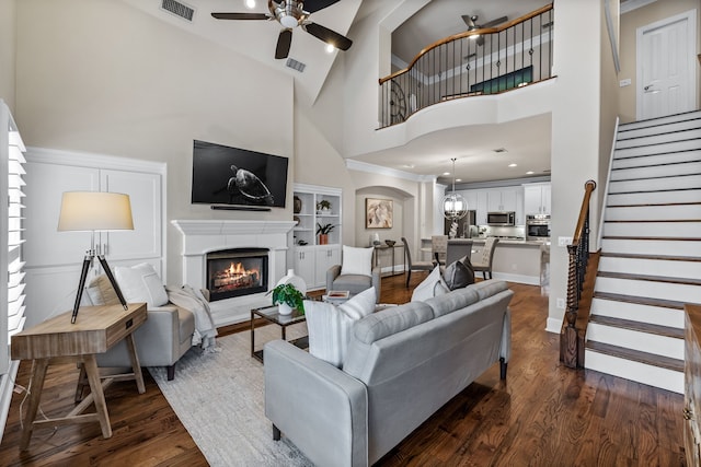 living room with built in shelves, ceiling fan, dark hardwood / wood-style flooring, and high vaulted ceiling