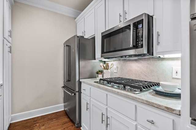 kitchen with white cabinets, light stone countertops, ornamental molding, dark hardwood / wood-style flooring, and stainless steel appliances