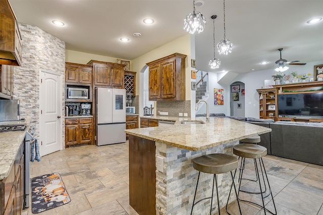 kitchen featuring sink, stainless steel appliances, tasteful backsplash, a breakfast bar area, and ceiling fan with notable chandelier