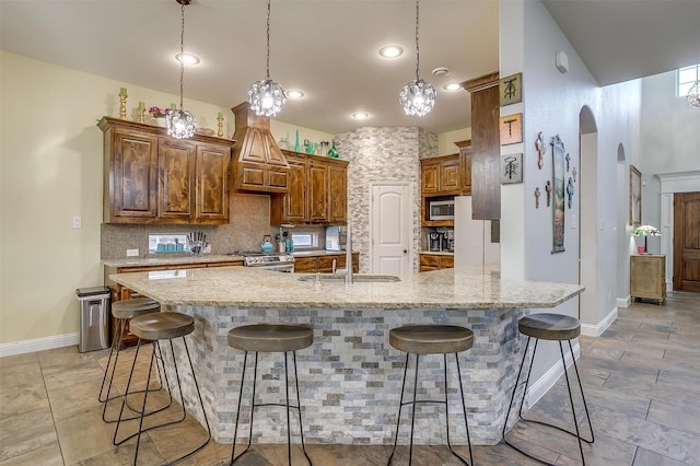 kitchen with sink, appliances with stainless steel finishes, decorative light fixtures, light stone counters, and a breakfast bar area