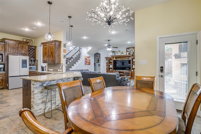 dining space with sink and ceiling fan with notable chandelier