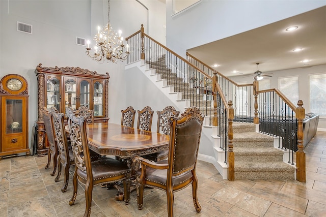 dining space featuring ceiling fan with notable chandelier and a high ceiling