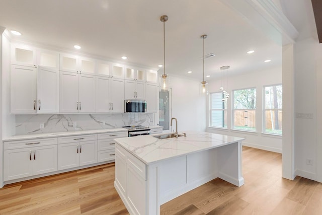 kitchen with pendant lighting, sink, stainless steel appliances, an island with sink, and white cabinets