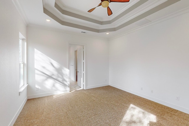 empty room with a raised ceiling, ceiling fan, carpet, and ornamental molding