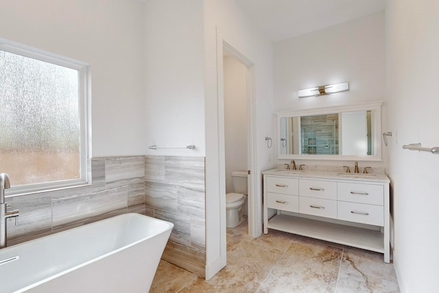 bathroom with a bathing tub, vanity, toilet, and tile walls