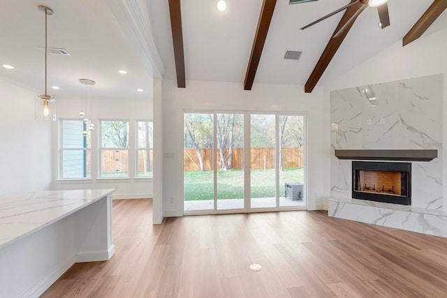 unfurnished living room featuring vaulted ceiling with beams, a high end fireplace, ceiling fan, and light wood-type flooring