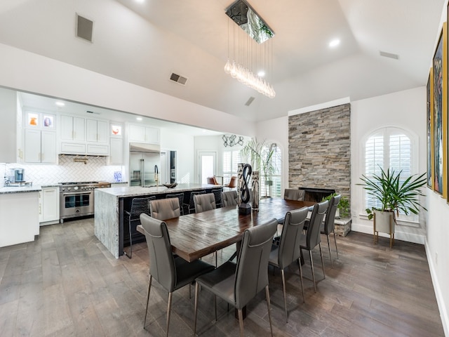 dining room with a fireplace, dark wood-type flooring, lofted ceiling, and a notable chandelier