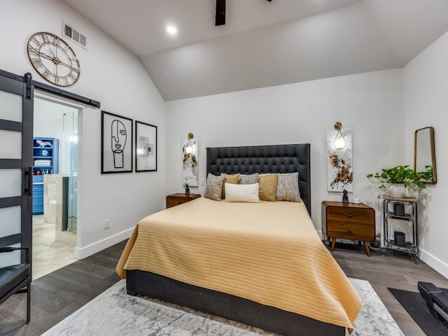 bedroom featuring a barn door, lofted ceiling, dark wood-type flooring, and connected bathroom