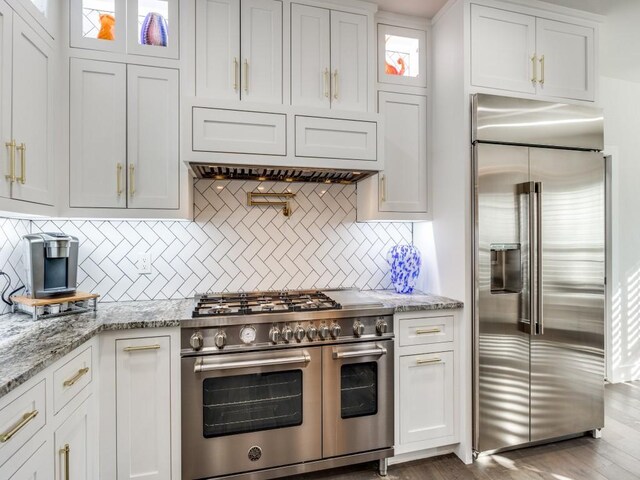 kitchen with light stone counters, high end appliances, white cabinetry, and backsplash