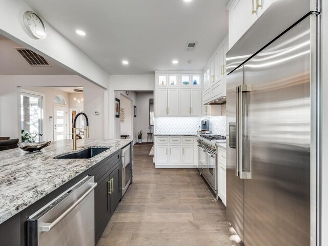 kitchen with light stone countertops, white cabinetry, sink, light hardwood / wood-style flooring, and high end appliances