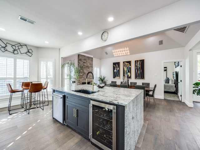 kitchen featuring light stone counters, sink, a center island with sink, light hardwood / wood-style flooring, and wine cooler