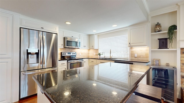 kitchen featuring white cabinets, dark stone countertops, stainless steel appliances, and beverage cooler