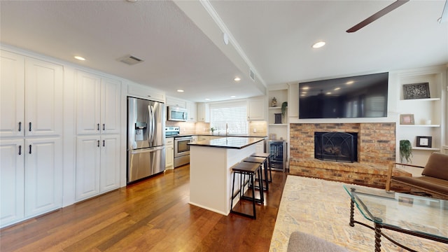 kitchen with a kitchen bar, white cabinetry, appliances with stainless steel finishes, and dark hardwood / wood-style flooring