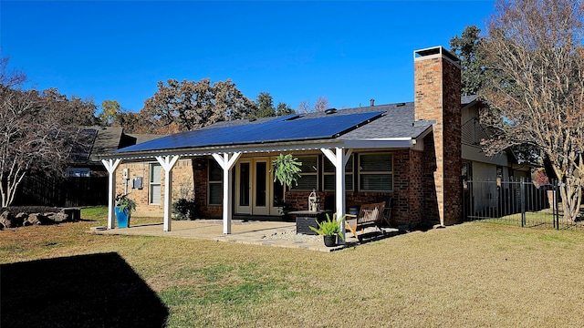 rear view of property featuring a lawn, a patio, a chimney, fence, and roof mounted solar panels