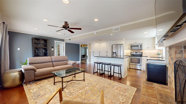 living room featuring ceiling fan, sink, crown molding, and hardwood / wood-style flooring