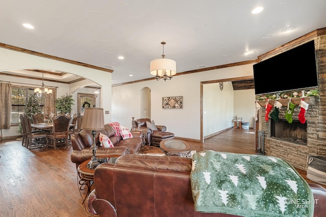 living room with an inviting chandelier, hardwood / wood-style flooring, a stone fireplace, and ornamental molding