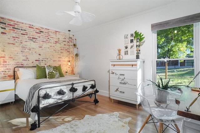 bedroom featuring ornamental molding, a ceiling fan, brick wall, and wood finished floors