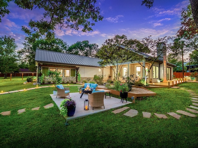 back of property at dusk with a lawn, a chimney, metal roof, an outdoor hangout area, and a standing seam roof