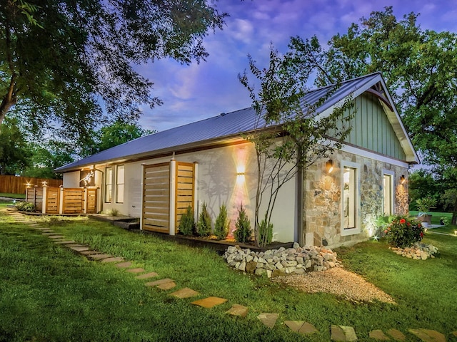 view of property exterior with a lawn, board and batten siding, fence, metal roof, and stone siding