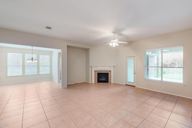 unfurnished living room with a tiled fireplace, ceiling fan with notable chandelier, and light tile patterned floors