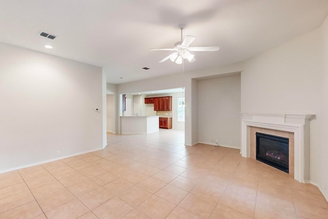 unfurnished living room featuring ceiling fan, a tiled fireplace, and light tile patterned floors